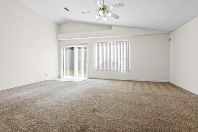 an empty room with a chandelier fan and windows