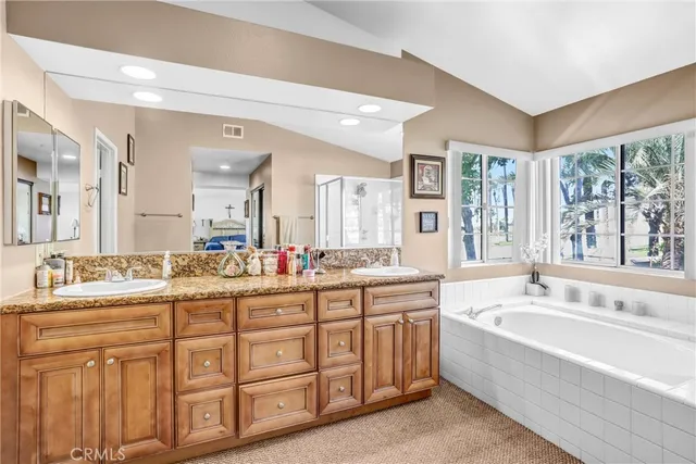 a bathroom with a granite countertop double vanity sink a large mirror a bathtub and next to a window