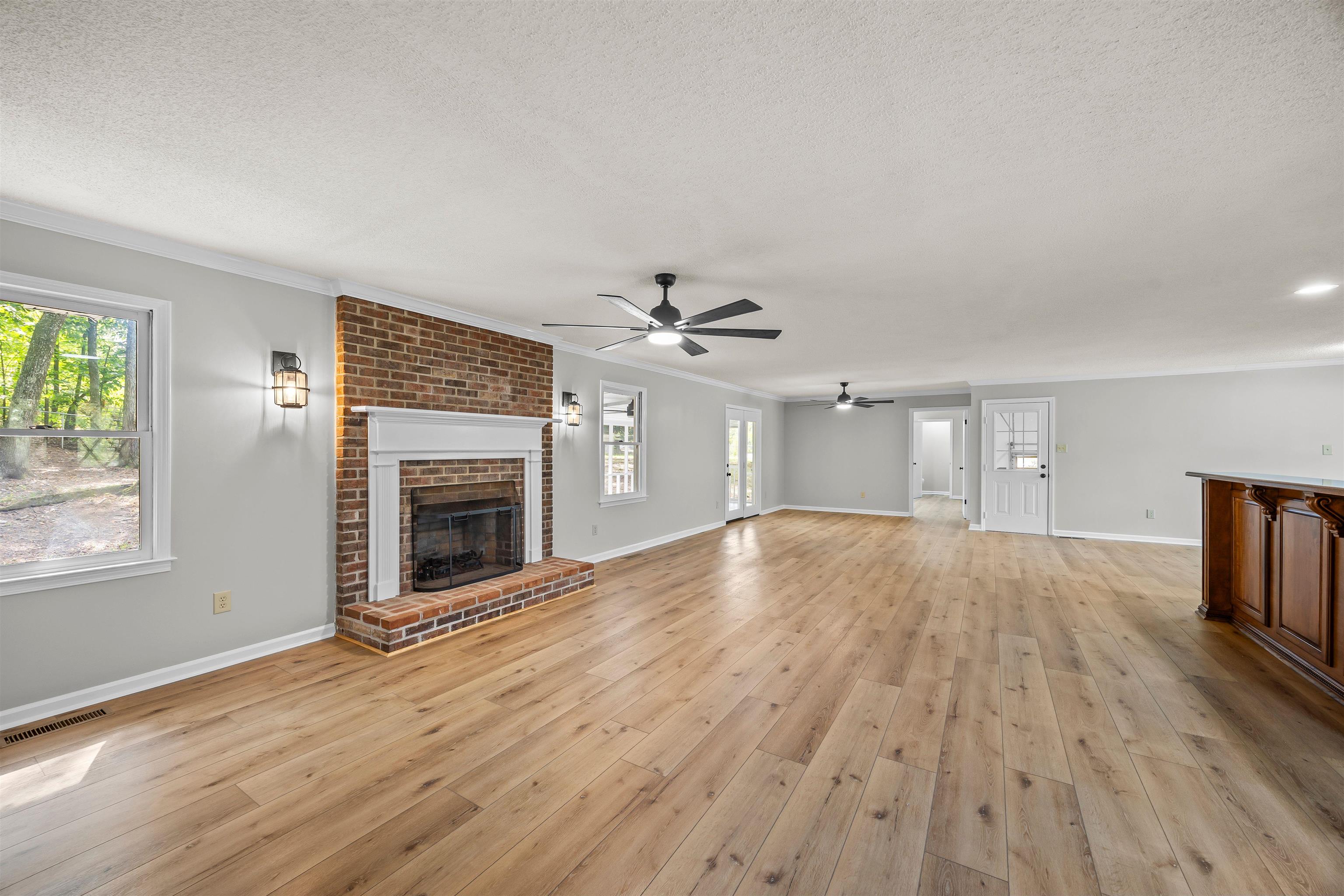 80 Pinewood Drive Jackson, TN 38305 - Photo 3 of 27 Unfurnished living room featuring a brick fireplace, crown molding, a textured ceiling, light wood-style floors, and a ceiling fan