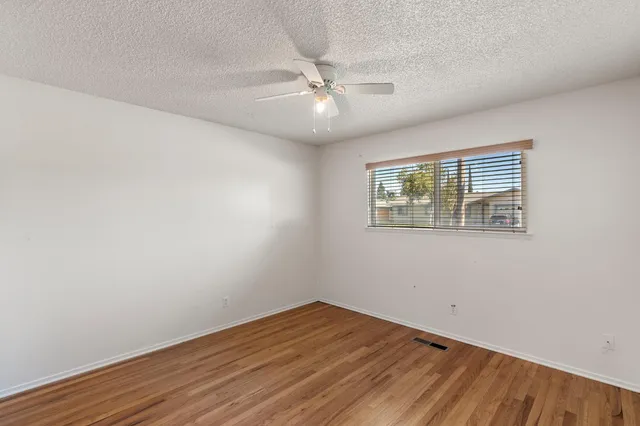 an empty room with wooden floor fan and windows
