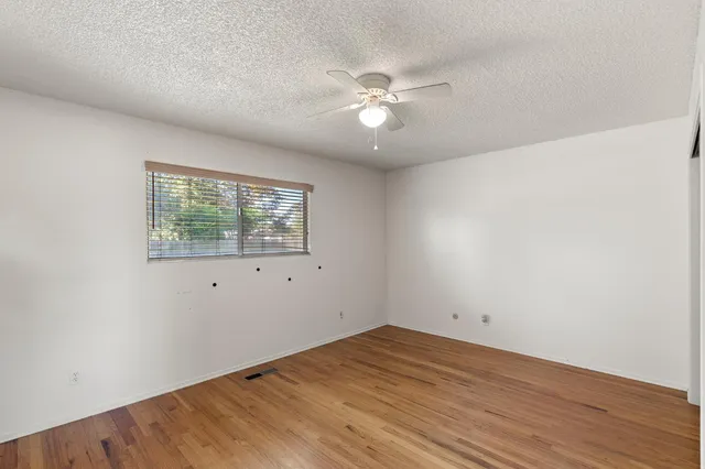 an empty room with wooden floor fan and windows