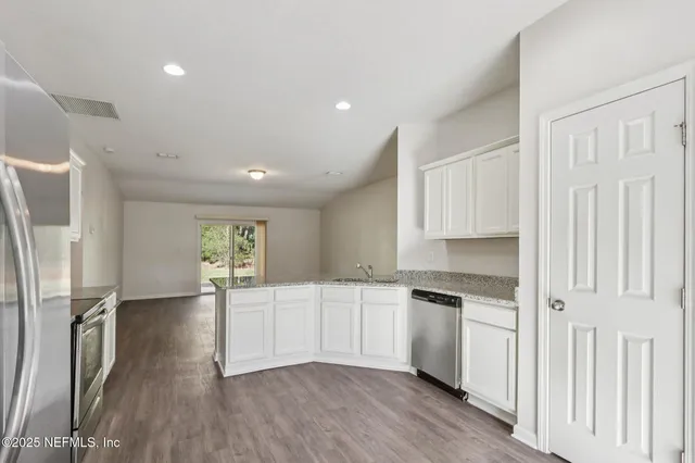 a kitchen with granite countertop a refrigerator a sink dishwasher a stove and white cabinets with wooden floor