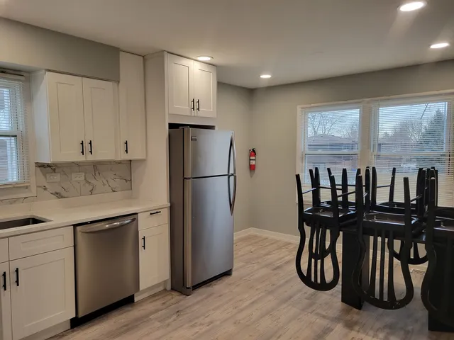a kitchen with stainless steel appliances granite countertop a dining table chairs refrigerator and cabinets