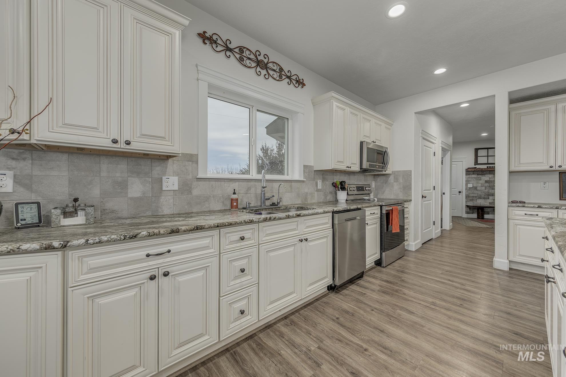5631 Sunset Road Fruitland, ID 83619 - Photo 15 of 50 Kitchen with white cabinetry, appliances with stainless steel finishes, light wood-style flooring, backsplash, and recessed lighting