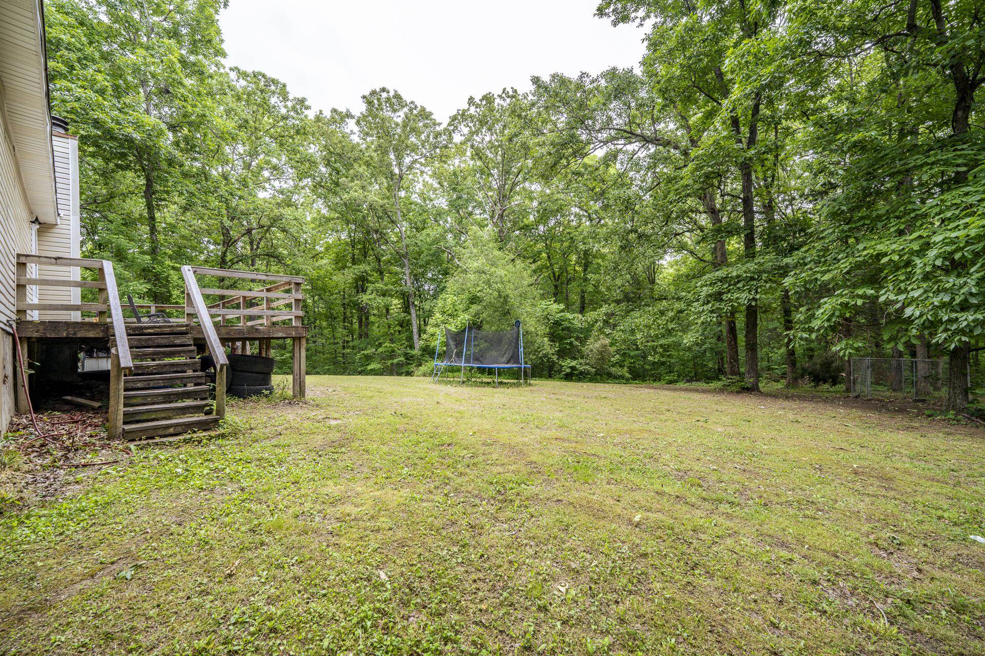 259 Oakview Drive Adamsville, TN 38310 - Photo 25 of 32 Expansive rear yard featuring a wood-tone deck with stairs and railing, a broad lawn, and mature trees providing natural screening