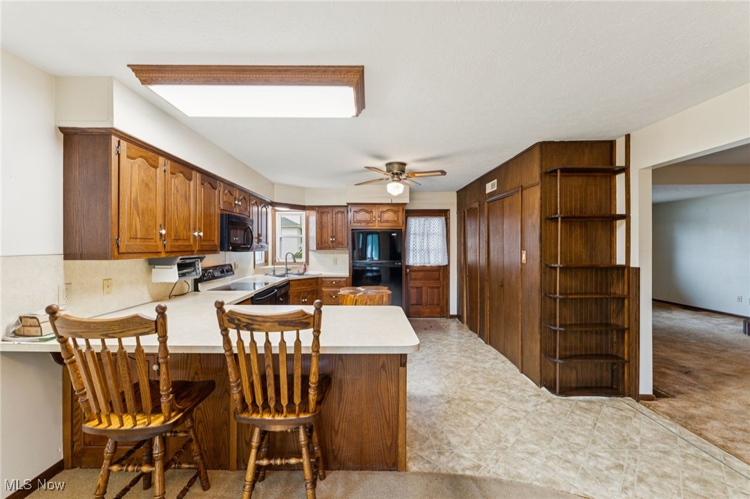 12422 Portage Street Rittman, OH 44270 - Photo 11 of 42 Kitchen featuring light countertops, brown cabinets, black appliances, a peninsula, and a kitchen bar