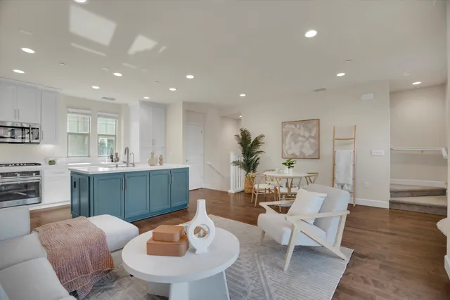 a living room with stainless steel appliances furniture a rug and a kitchen view