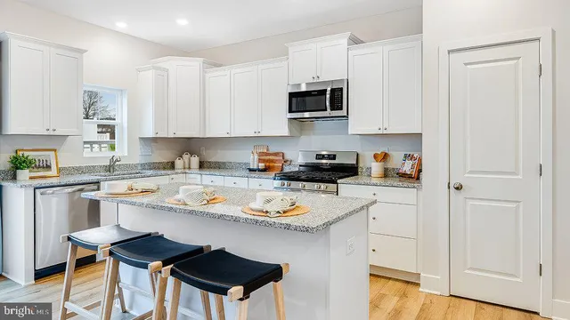 a white kitchen with a stove a sink dishwasher and a refrigerator with wooden floor