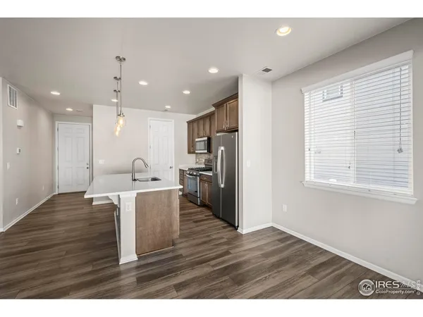 a view of kitchen with stainless steel appliances granite countertop a refrigerator a sink a stove and a wooden floors
