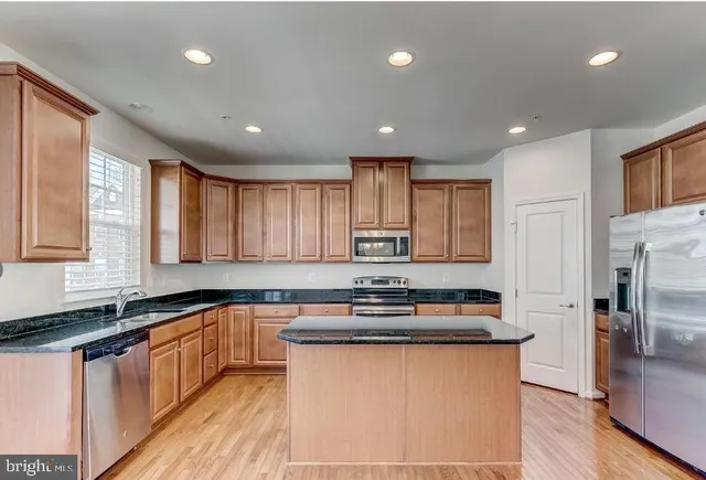 a kitchen with stainless steel appliances granite countertop a sink a stove a refrigerator a center island and a window