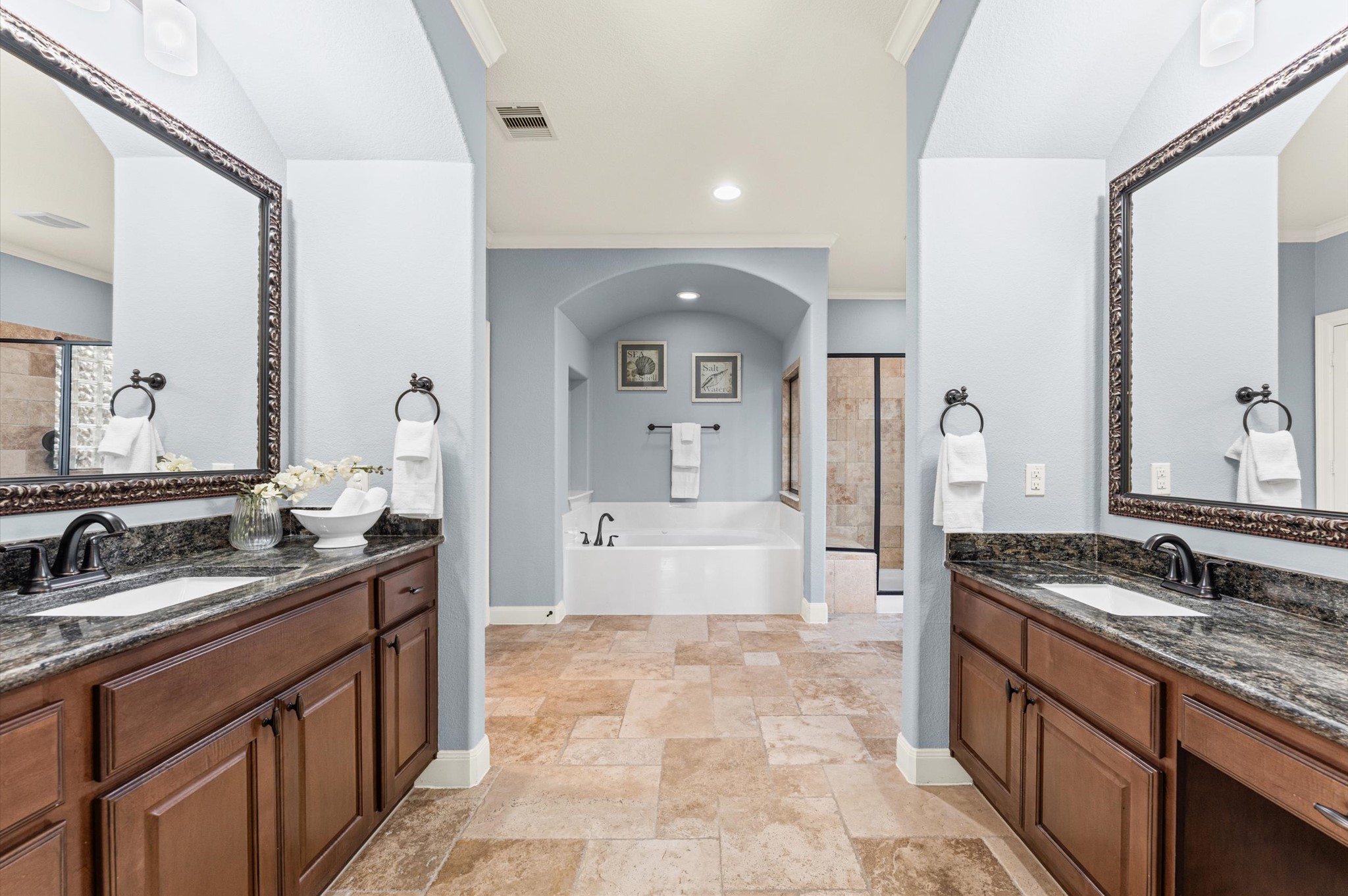 70 Valera Ridge Drive Spring, TX 77389 - Photo 24 of 37 This spacious bathroom features dual vanities with dark granite countertops and elegant wood cabinetry. It has a central soaking tub, a separate shower, and soft blue-gray walls, creating a serene and inviting atmosphere.