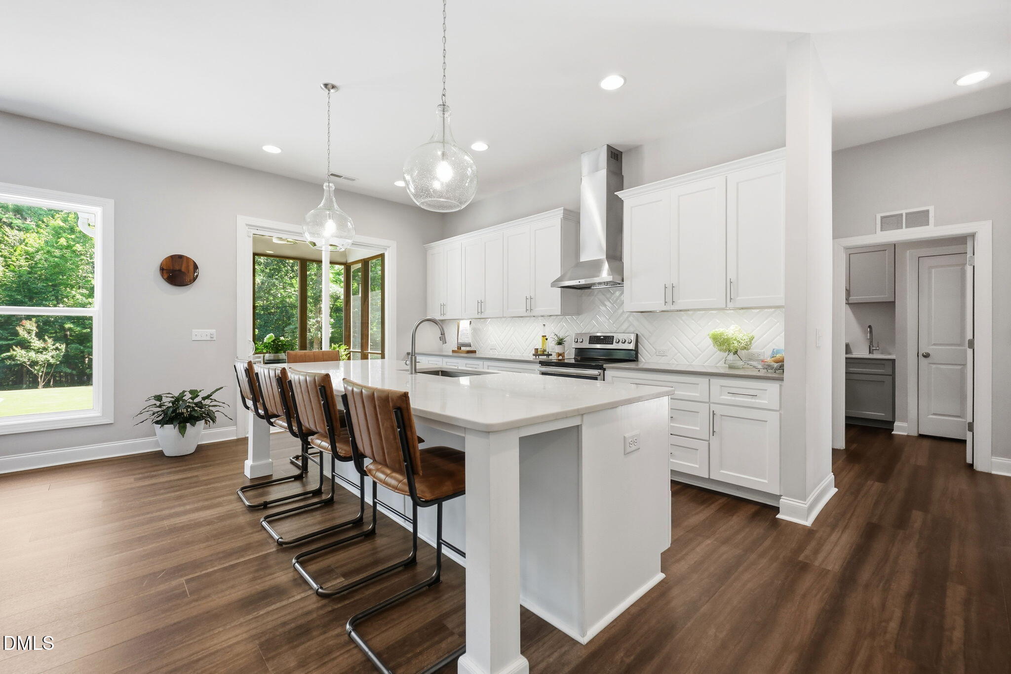 2513 Countrywood Road Raleigh, NC 27615 - Photo 4 of 50 Modern kitchen featuring white cabinetry, stainless steel appliances, a herringbone tile backsplash, range hood, and a large center island.