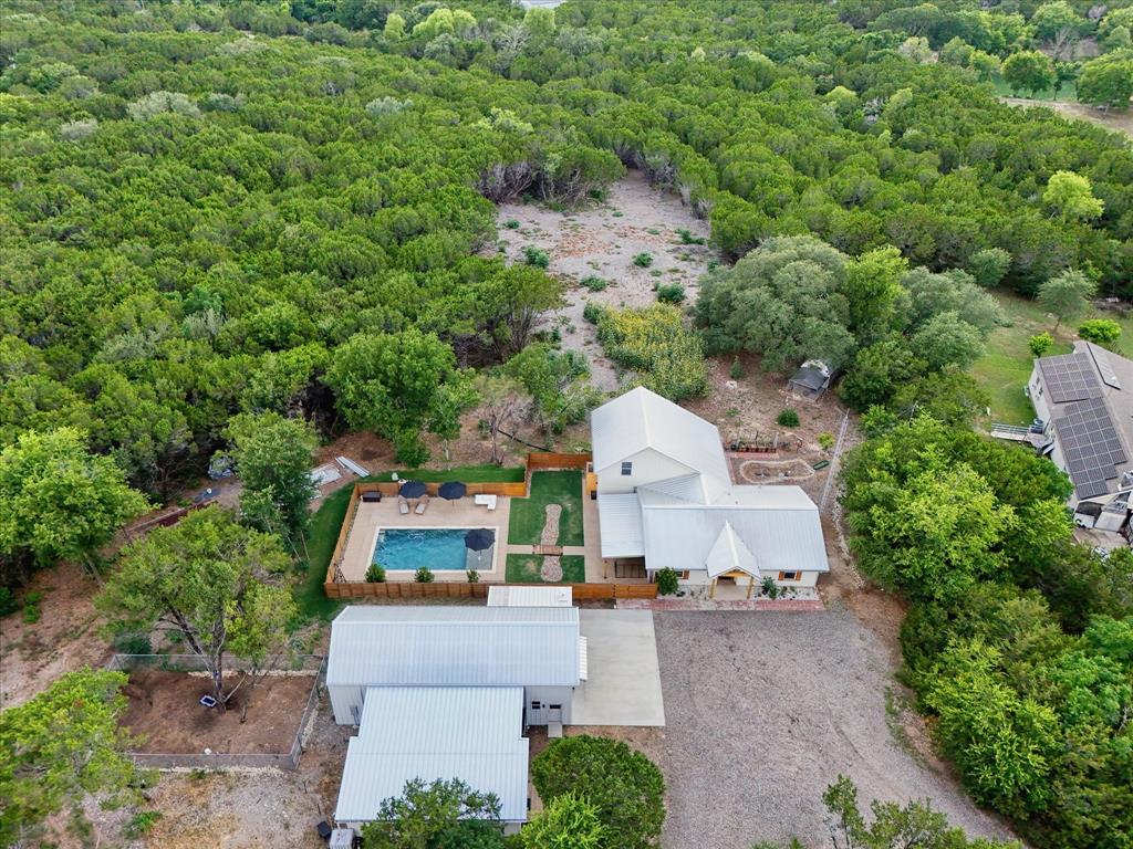Aerial perspective showcasing a modern farmhouse-style residence with a detached garage building, surrounded by dense natural landscaping
