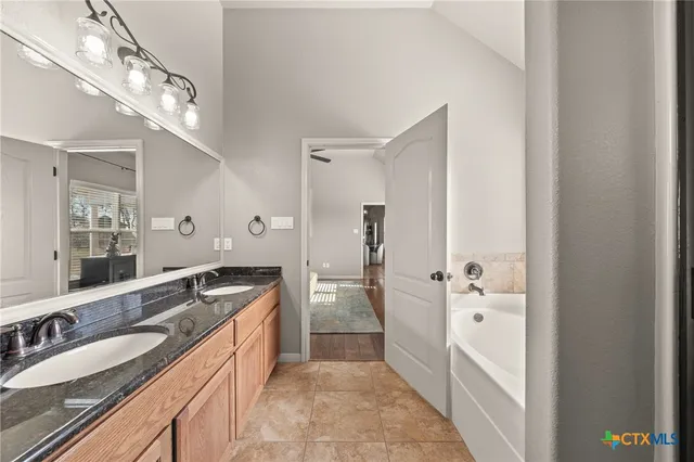 a spacious bathroom with a granite countertop double vanity sink a mirror and a bathtub