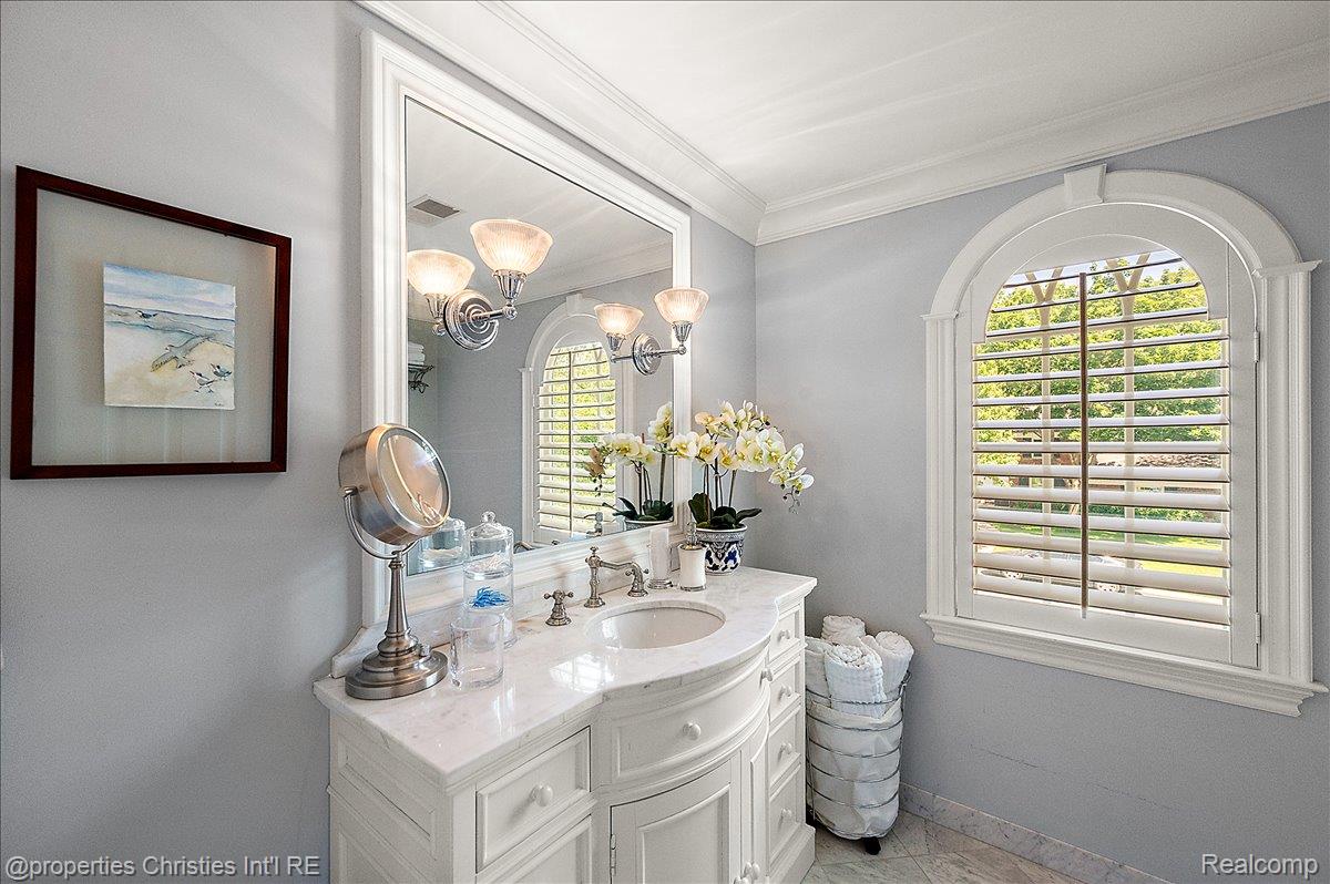 135 Clifton Road Bloomfield Hills, MI 48301 - Photo 53 of 77 Bathroom featuring a white vanity with an integrated basin, a polished stone countertop, a large framed mirror, and an arched window with plantation shutters
