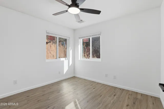 an empty room with wooden floor chandelier fan and windows
