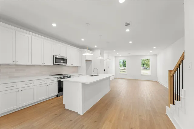 a large kitchen with stainless steel appliances a large counter top a sink a refrigerator and white cabinets