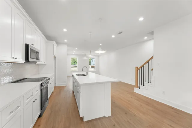 a large kitchen with stainless steel appliances a sink a oven a stove and a wooden floors