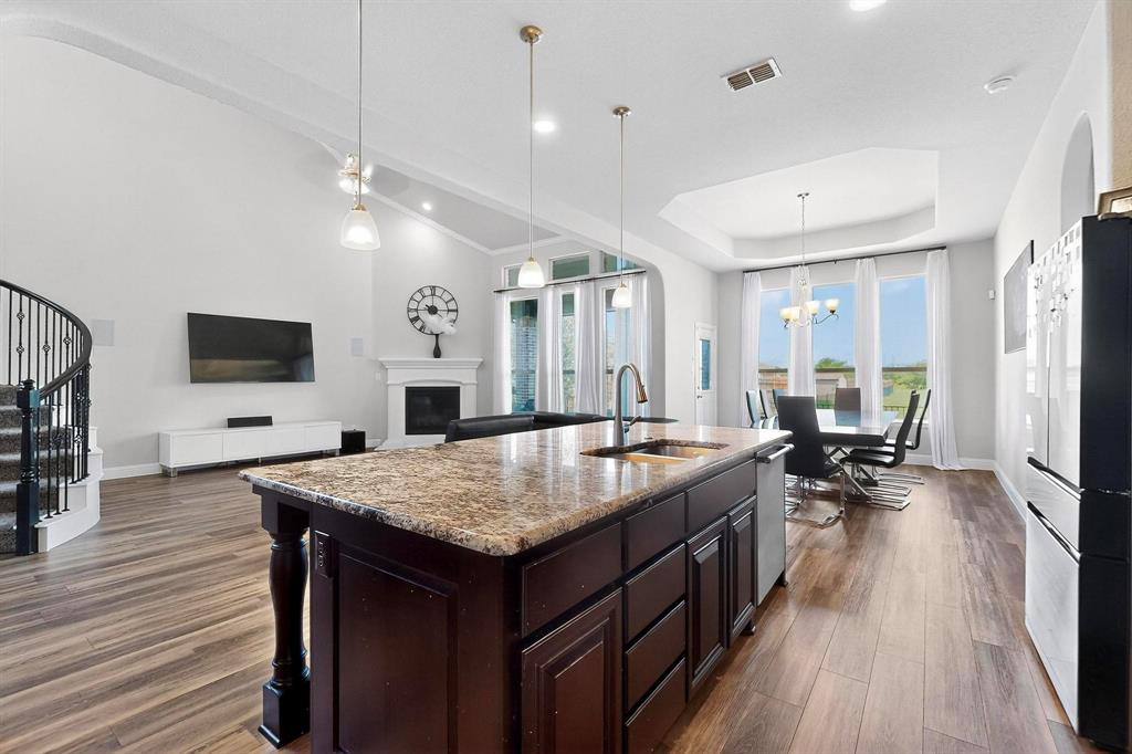 2549 Boot Jack Road Fort Worth, TX 76177 - Photo 4 of 13 Kitchen with dark brown cabinetry, a glass covered fireplace, pendant lighting, light stone countertops, and freestanding refrigerator
