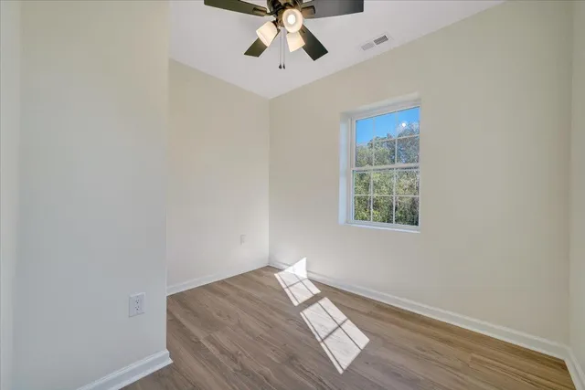 an empty room with wooden floor chandelier fan and windows