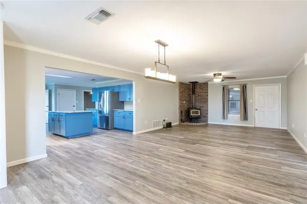 an empty room with wooden floor kitchen view and windows