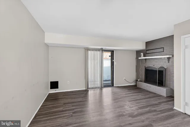 a view of an empty room with wooden floor fireplace and a window