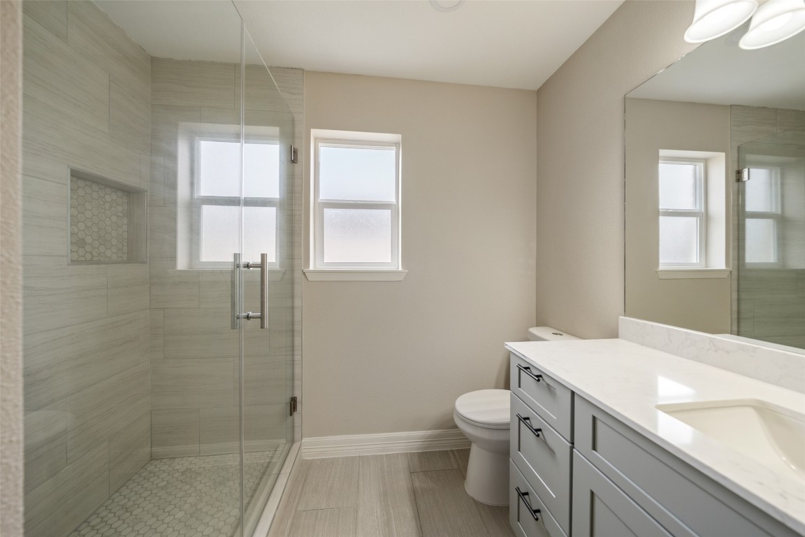 355 Windsor Square Alvin, TX 77511 - Photo 13 of 22 This bathroom features a modern design with a glass-enclosed shower, a large mirror, and a sleek vanity with ample storage. The neutral color palette and natural light from the window create a bright and inviting space.