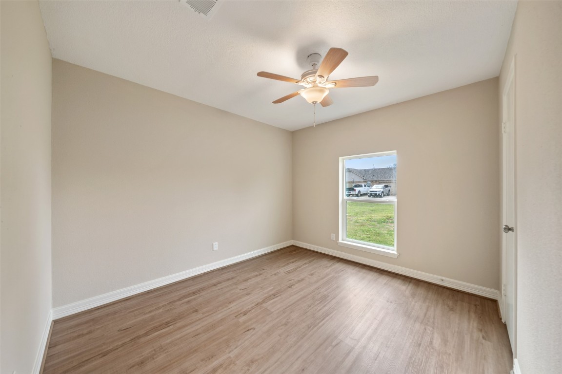 355 Windsor Square Alvin, TX 77511 - Photo 15 of 22 This photo showcases a bright, unfurnished room with neutral-colored walls and wood-look flooring. A ceiling fan is centrally located, and a window provides natural light with a view of the outside.