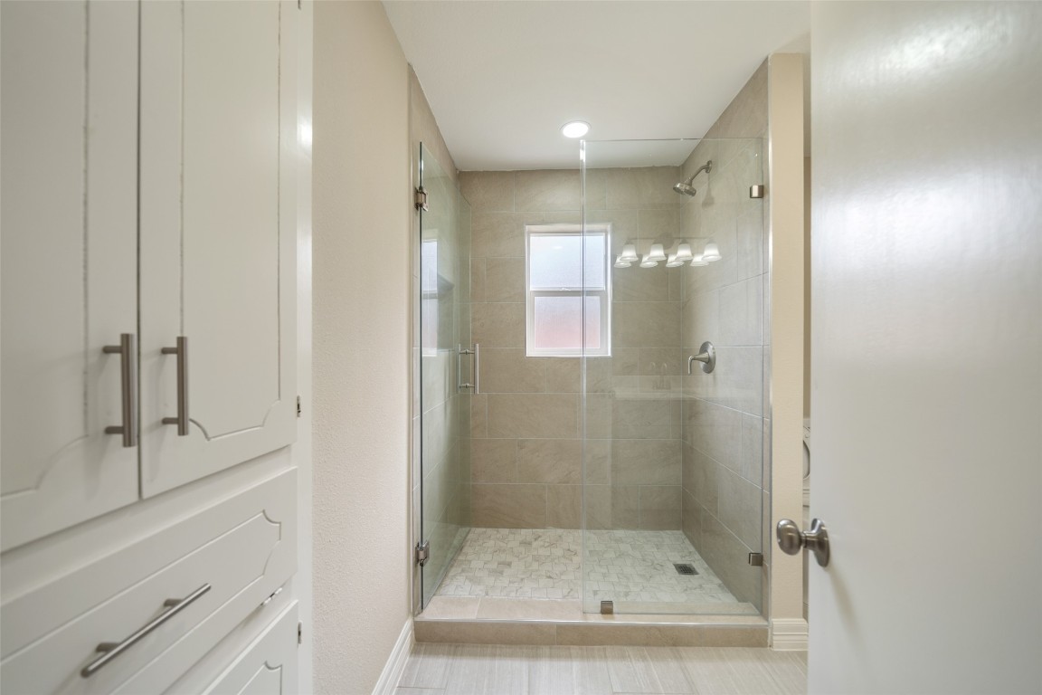 355 Windsor Square Alvin, TX 77511 - Photo 16 of 22 This modern bathroom features a spacious glass-enclosed shower with elegant tile work and a window for natural light. Ample storage is provided by the built-in cabinets with sleek hardware.