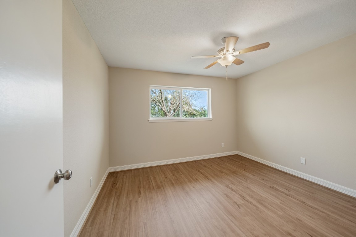 355 Windsor Square Alvin, TX 77511 - Photo 18 of 22 This is a bright, unfurnished bedroom with neutral walls, wood-style flooring, a ceiling fan, and a window providing natural light and a view of greenery.