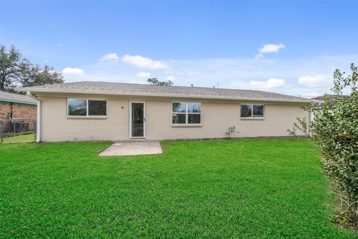 355 Windsor Square Alvin, TX 77511 - Photo 21 of 22 This photo shows the back of a single-story house with a light-colored brick exterior. It features several windows and a central door leading to a spacious, well-maintained grassy backyard, perfect for outdoor activities and relaxation.