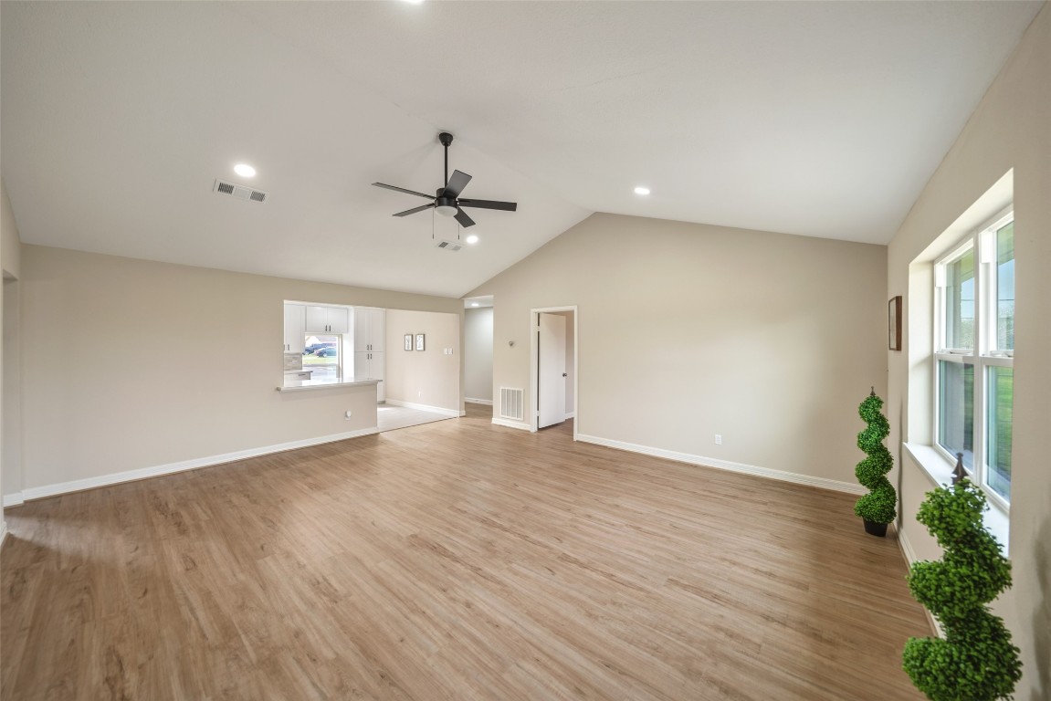 355 Windsor Square Alvin, TX 77511 - Photo 3 of 22 This spacious living area features a vaulted ceiling with recessed lighting and a modern ceiling fan. The room boasts large windows for natural light, hardwood floors, and neutral walls. It opens into a kitchen area, enhancing the open-concept layout.