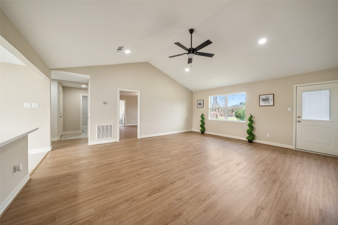 355 Windsor Square Alvin, TX 77511 - Photo 4 of 22 This spacious living area features a vaulted ceiling with a modern ceiling fan, large windows for natural light, and wood flooring. Neutral tones create a warm, inviting atmosphere with easy access to other rooms.