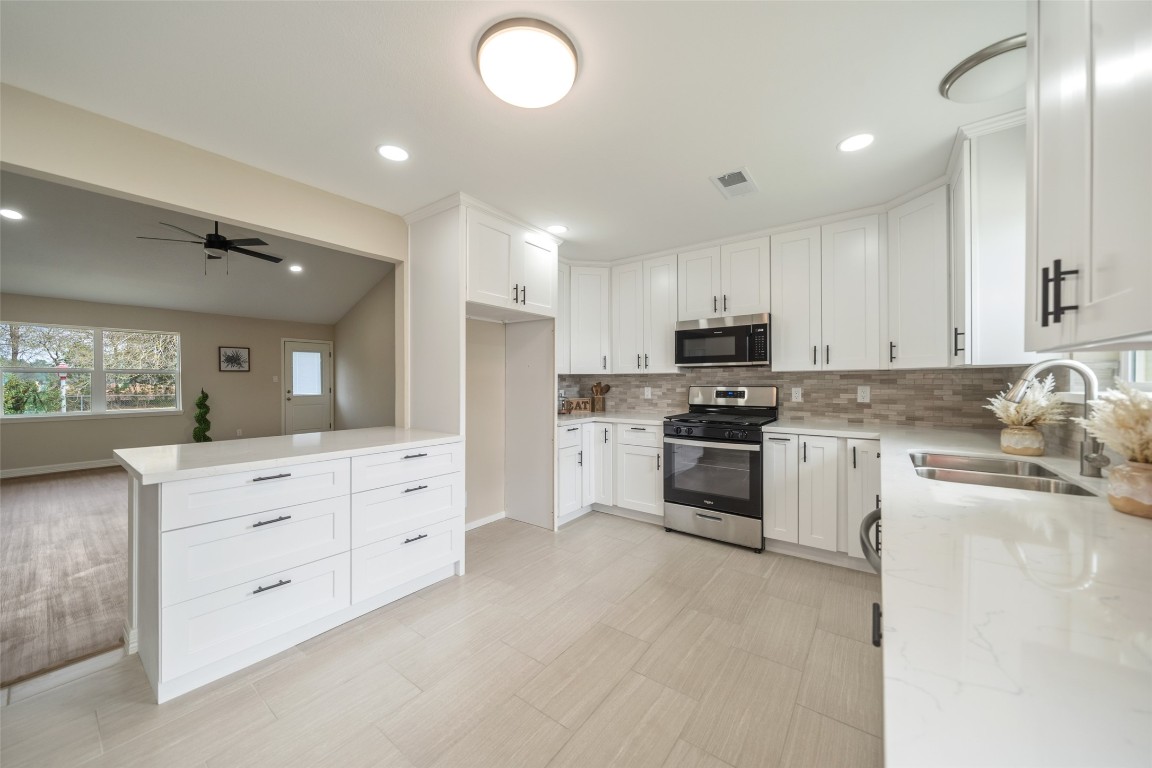 355 Windsor Square Alvin, TX 77511 - Photo 8 of 22 This spacious, modern kitchen features sleek white cabinetry, stainless steel appliances, and a stylish tile backsplash. The open layout flows into a bright living area with large windows and a ceiling fan, creating a welcoming and functional space for cooking and entertaining.