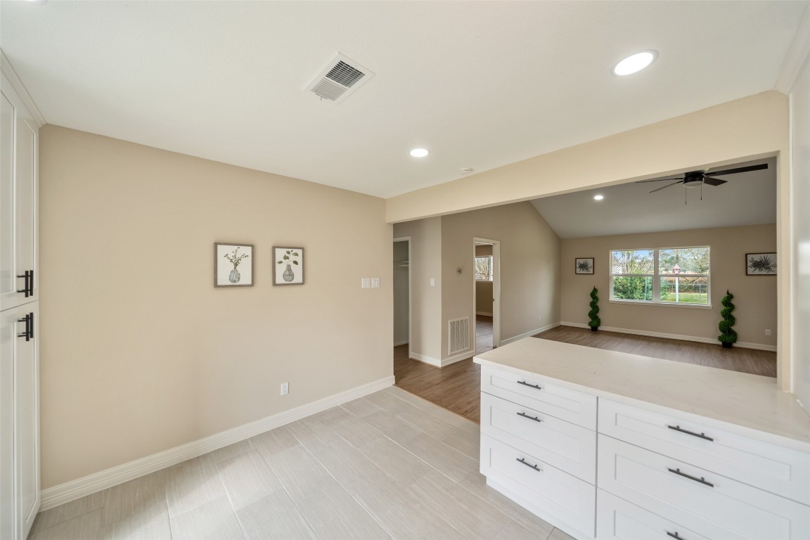 355 Windsor Square Alvin, TX 77511 - Photo 9 of 22 Bright, open-plan space with neutral walls and tile flooring. Features a transition from a kitchen area with white cabinetry to a living area with wood floors, ceiling fan, and large windows offering garden views.