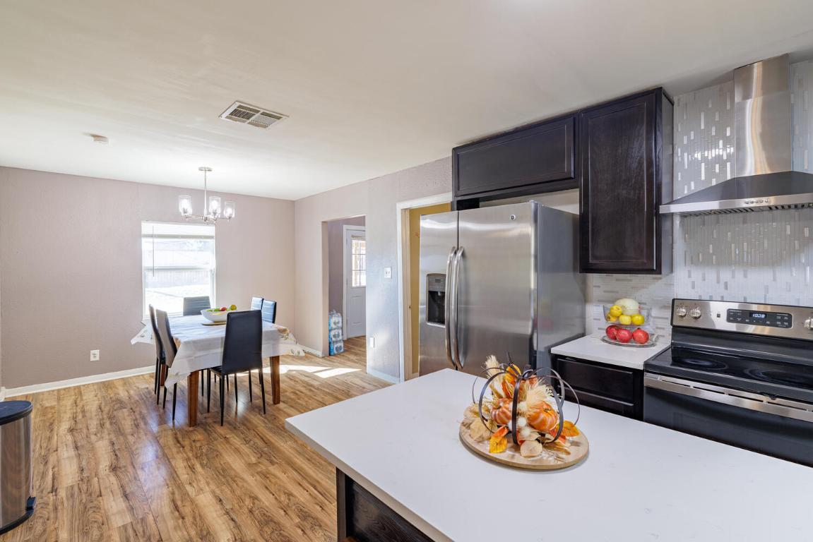 112 Maynard Street Bastrop, TX 78602 - Photo 12 of 35 Kitchen with wall chimney exhaust hood, stainless steel appliances, light wood-type flooring, decorative backsplash, and decorative light fixtures
