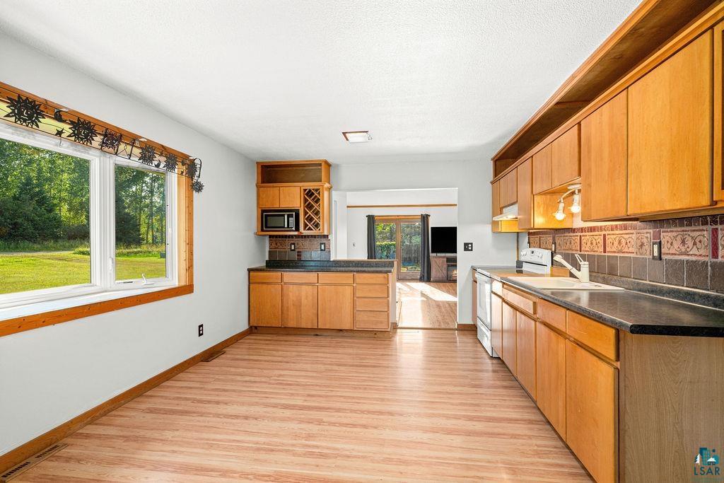 3949 East County Rd B Superior, WI 54880 - Photo 25 of 50 Wood-finish flooring, ample natural light from a large window, extensive wood cabinetry, dark countertops, and a tiled backsplash