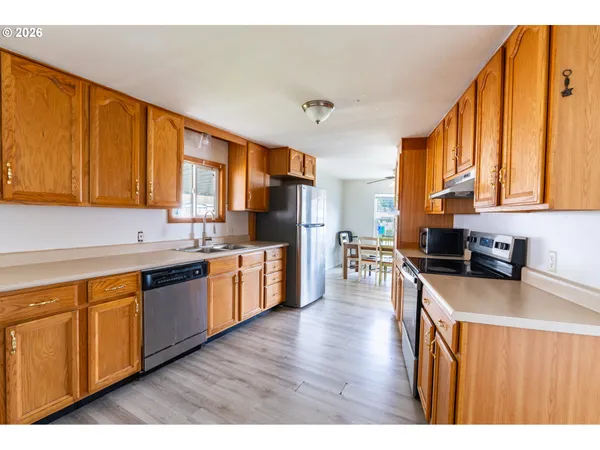 a kitchen with stainless steel appliances granite countertop wooden cabinets a refrigerator a stove a sink and dishwasher with wooden floor