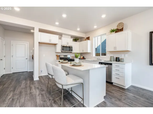 a kitchen with kitchen island granite countertop a sink a stove a refrigerator and white cabinets with wooden floor