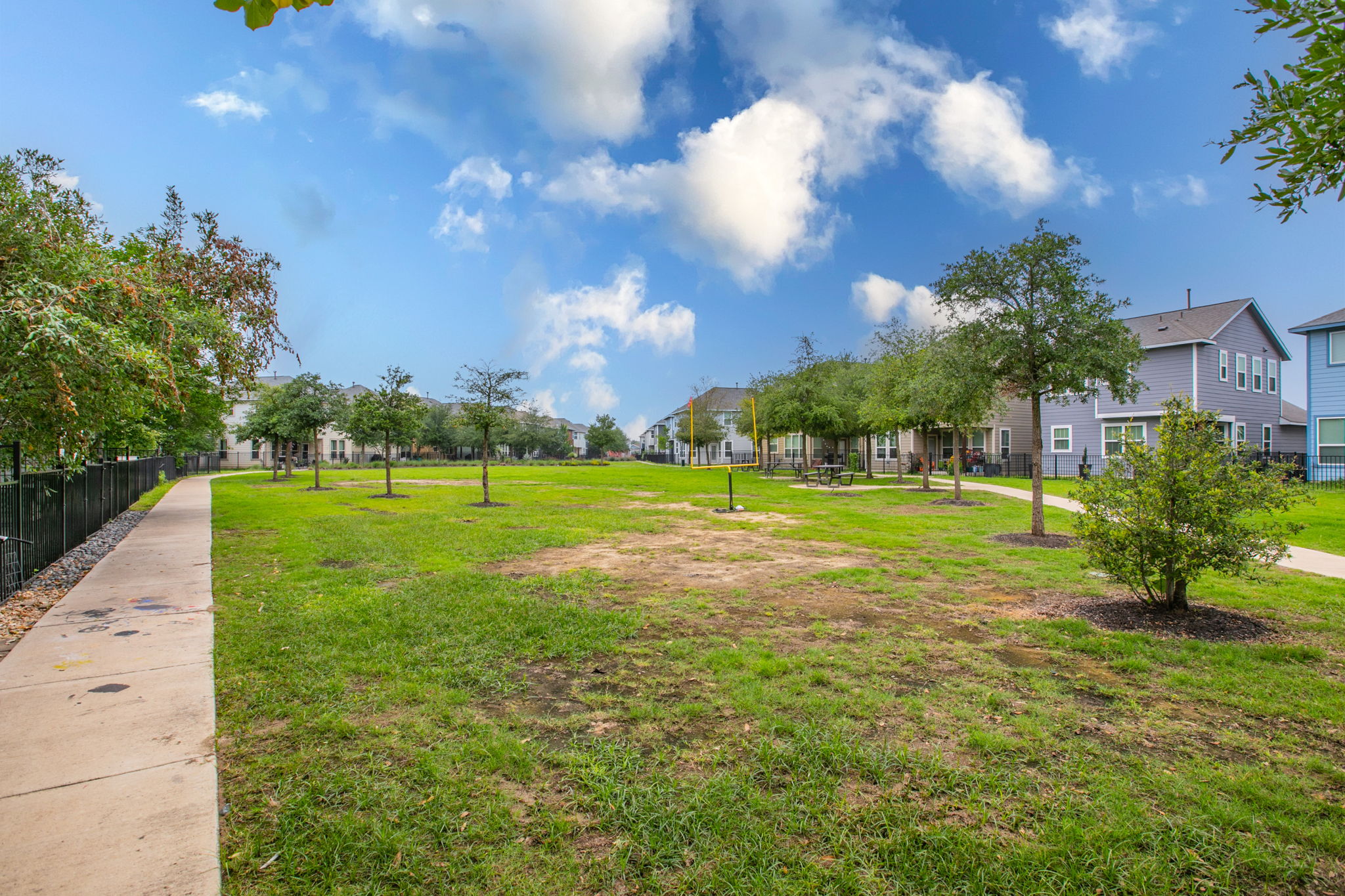 231 Simon Kyle, TX 78640 - Photo 28 of 29 Expansive greenspace featuring a meandering concrete path, mature trees, and a black metal fence