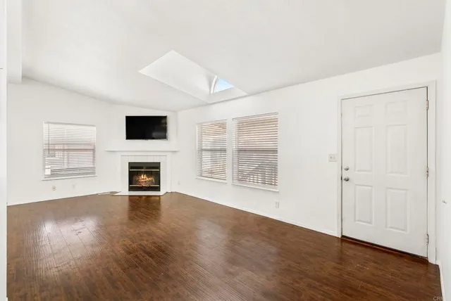 an empty room with wooden floor fireplace and windows