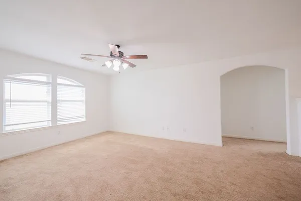 an empty room with chandelier fan and windows