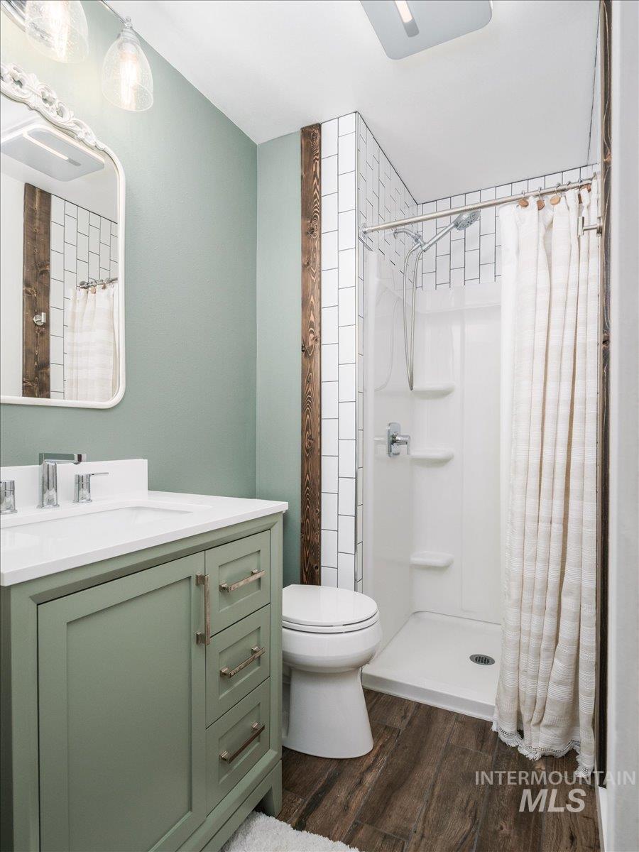1401 Chokecherry Drive Pocatello, ID 83204 - Photo 20 of 46 Bathroom featuring a sage green vanity with a white countertop and brushed nickel hardware, wood-finish flooring, a white toilet, and a shower with white subway tile surround