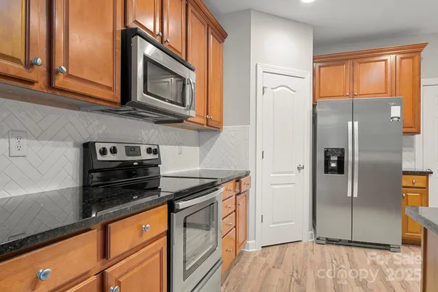 a kitchen with stainless steel appliances granite countertop a refrigerator a stove and a sink with wooden floor