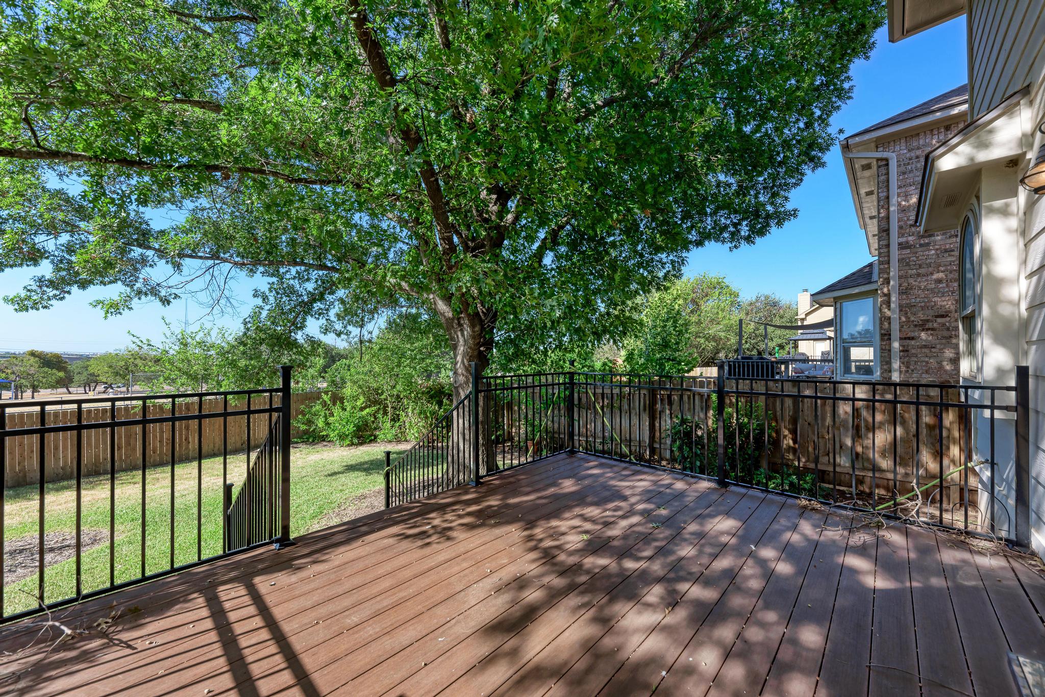 906 Antelope Ridge Cedar Park, TX 78613 - Photo 34 of 40 Shaded wooden deck overlooks a fenced grassy yard framed by mature green trees.