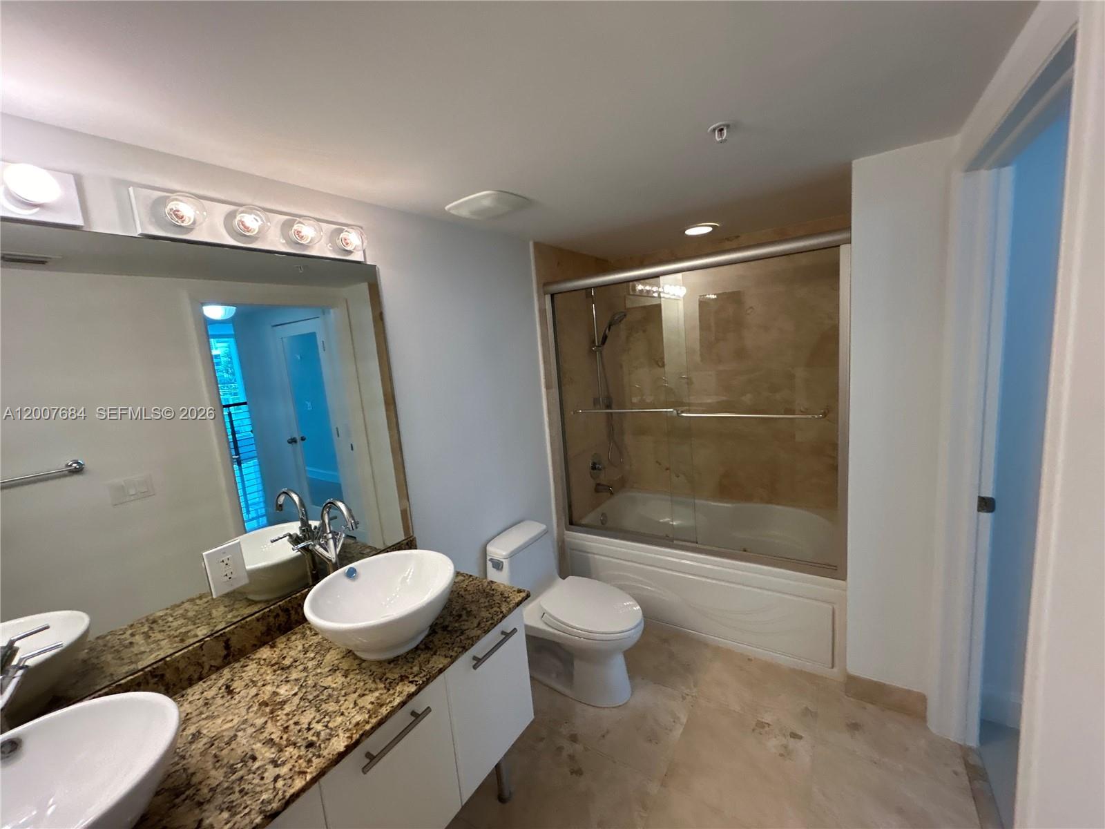 41 Southeast 5th Street, Unit 703 Miami, FL 33131 - Photo 11 of 18 a bathroom with a granite countertop sink a toilet a mirror and shower