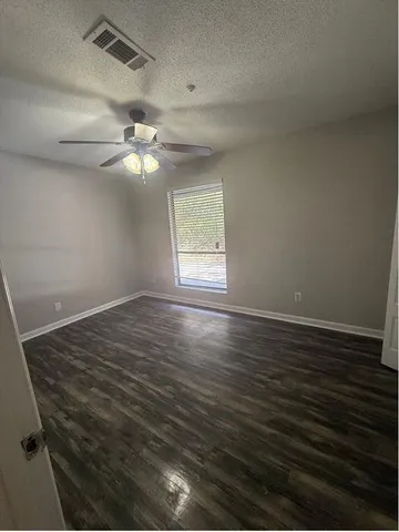 an empty room with wooden floor ceiling fan and window