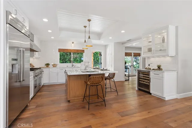 a kitchen with stainless steel appliances kitchen island granite countertop a stove a sink a refrigerator and white cabinets with wooden floor