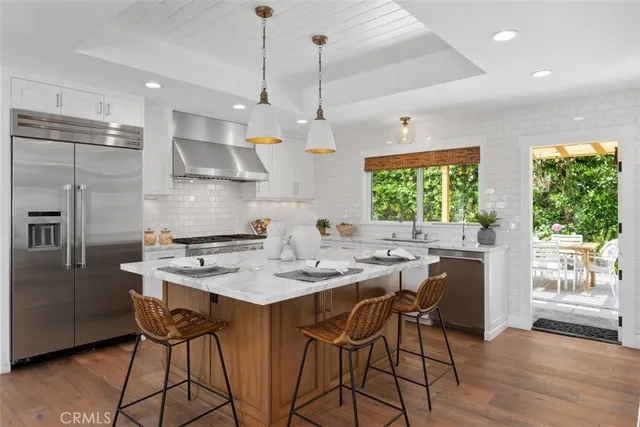 a kitchen with stainless steel appliances granite countertop a stove a refrigerator a sink a dining table and chairs with wooden floor