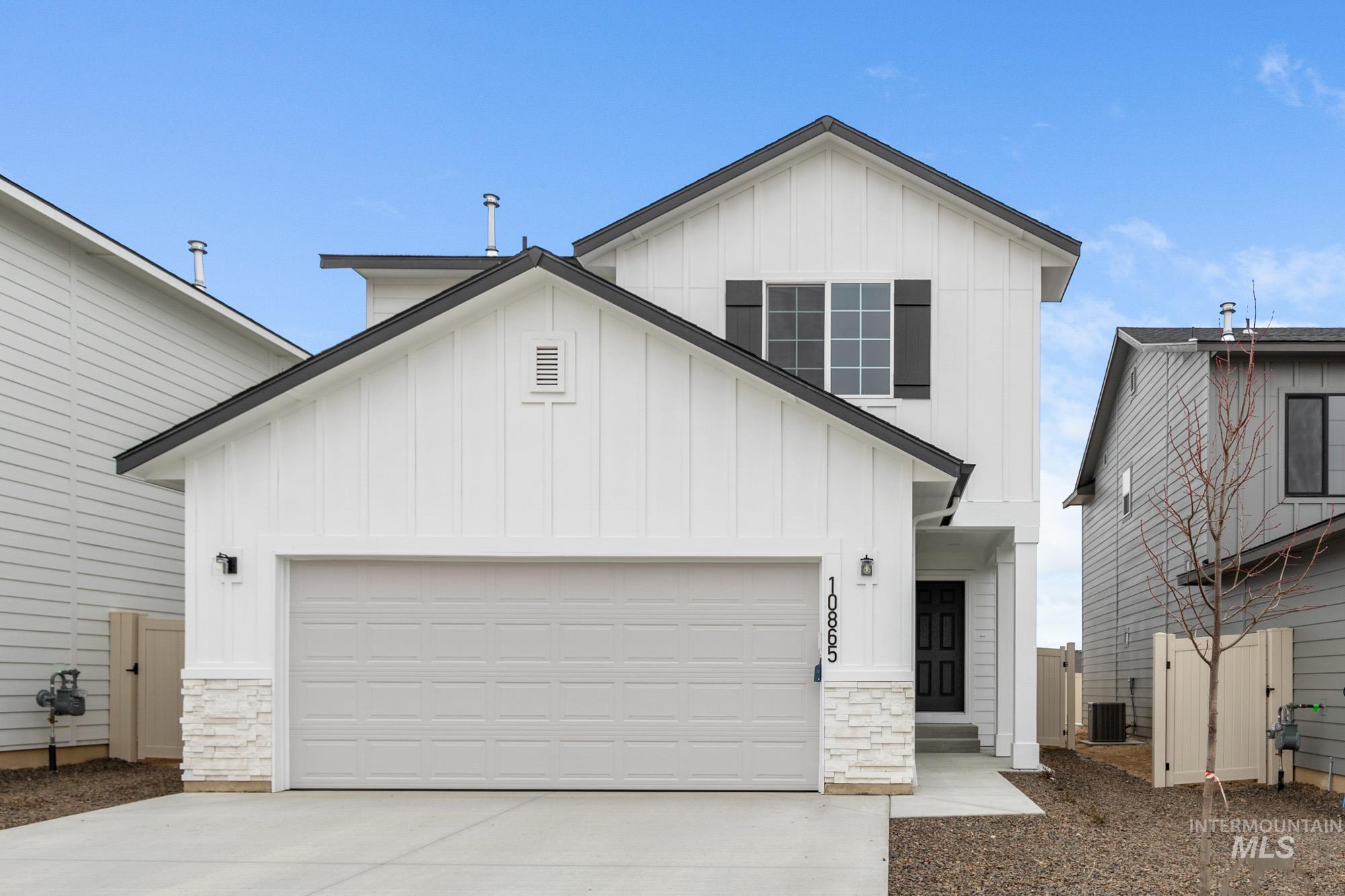 Modern farmhouse with board and batten siding, stone siding, driveway, and a garage